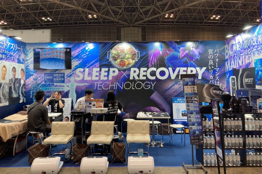 プロラボホールディングスの展示ブース全景。睡眠中の水分子に働きかける「WOTT」や、足裏から深部を温める「テラヘルツプロ」など、注目のセルフケア機器をスタイリッシュに展示。内側から整えるというブランドの世界観を表現していた。
